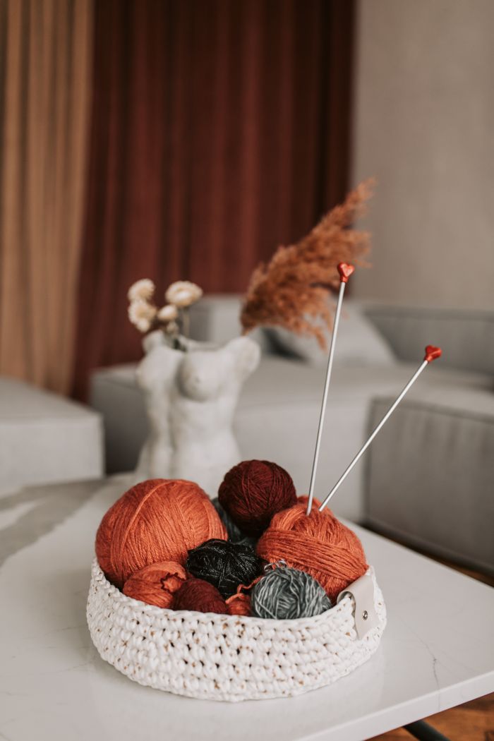 Aesthetic arrangement of yarn balls in a crochet basket with knitting needles for a cozy crafting ambiance.